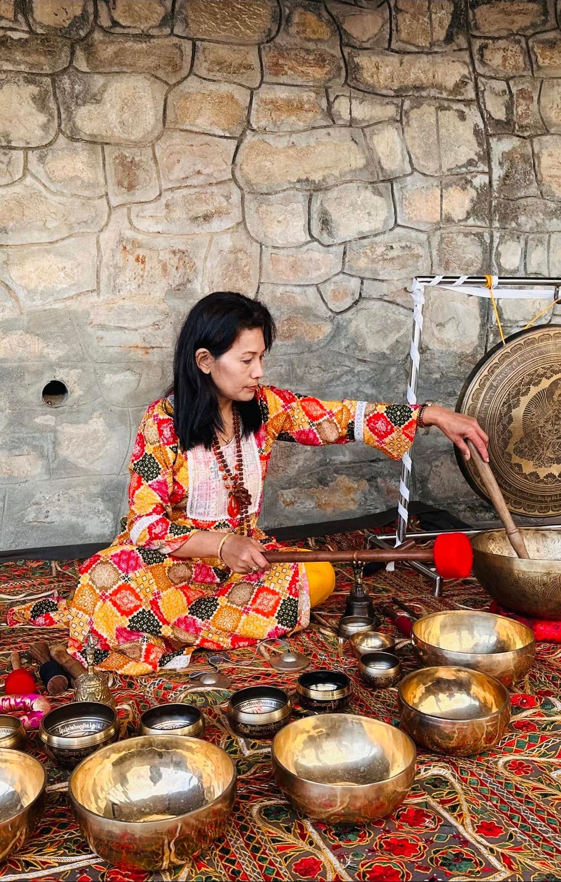 Babita Gurung playing a gong beside a full set of Himalayan singing bowls